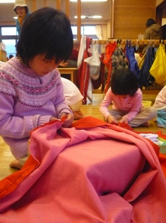 女の子は、自分のスカートを一針一針、集中して縫い上げます。